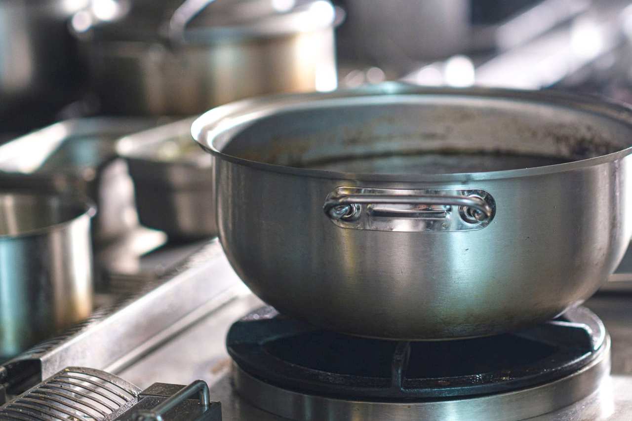 Cazuela de acero sobre el fuego de una cocina profesional, junto a la cesta de la freidora.